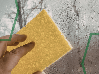 A picture showing a window covered in condensation. The window is being rubbed with a sponge.